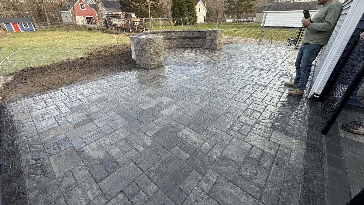 Large paver patio with a fire pit area and a seat wall in a backyard