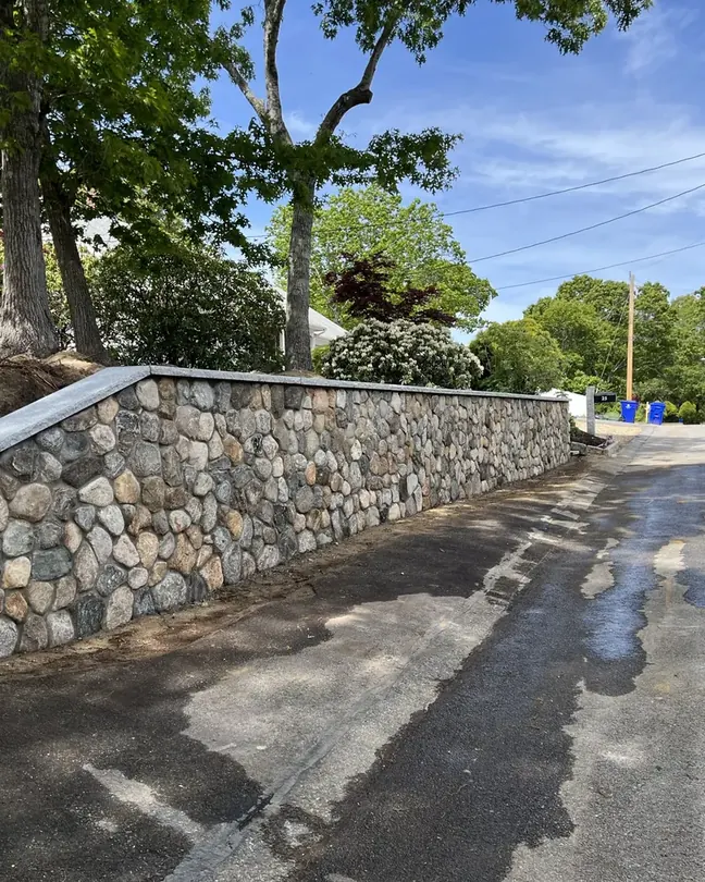 Long fieldstone retaining wall with a granite cap along a road