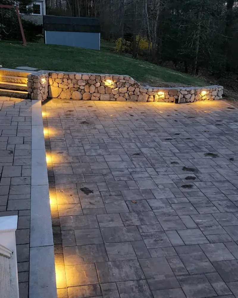 Paver patio and stone wall lit at night by built-in step lights