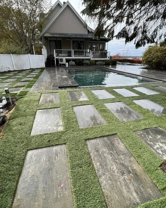 Large-format paver pool deck with grass joints next to an inground pool