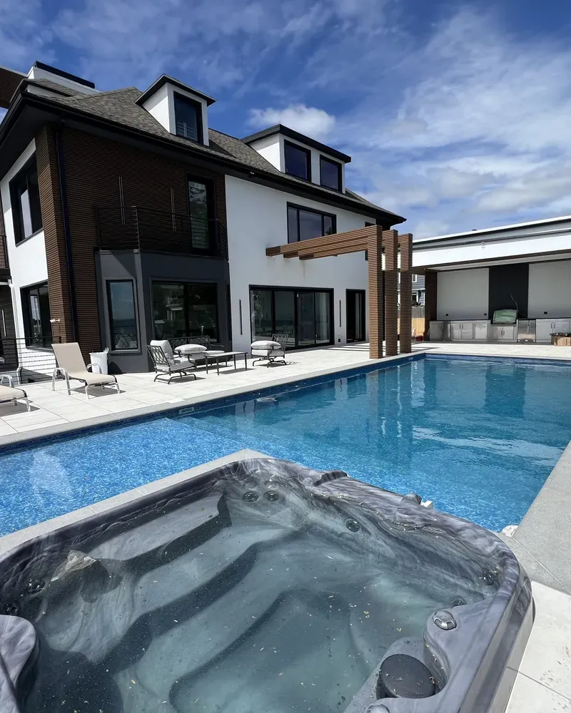 Light paver pool deck around an inground pool and spa behind a modern home