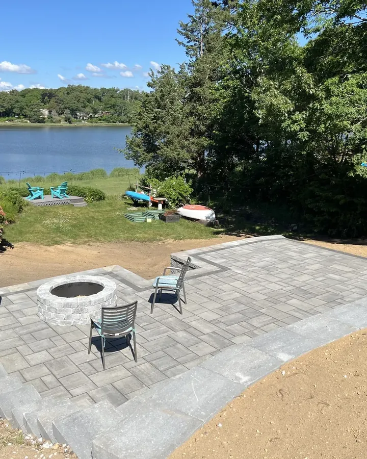 Paver patio with a sunken fire pit and chairs overlooking the water