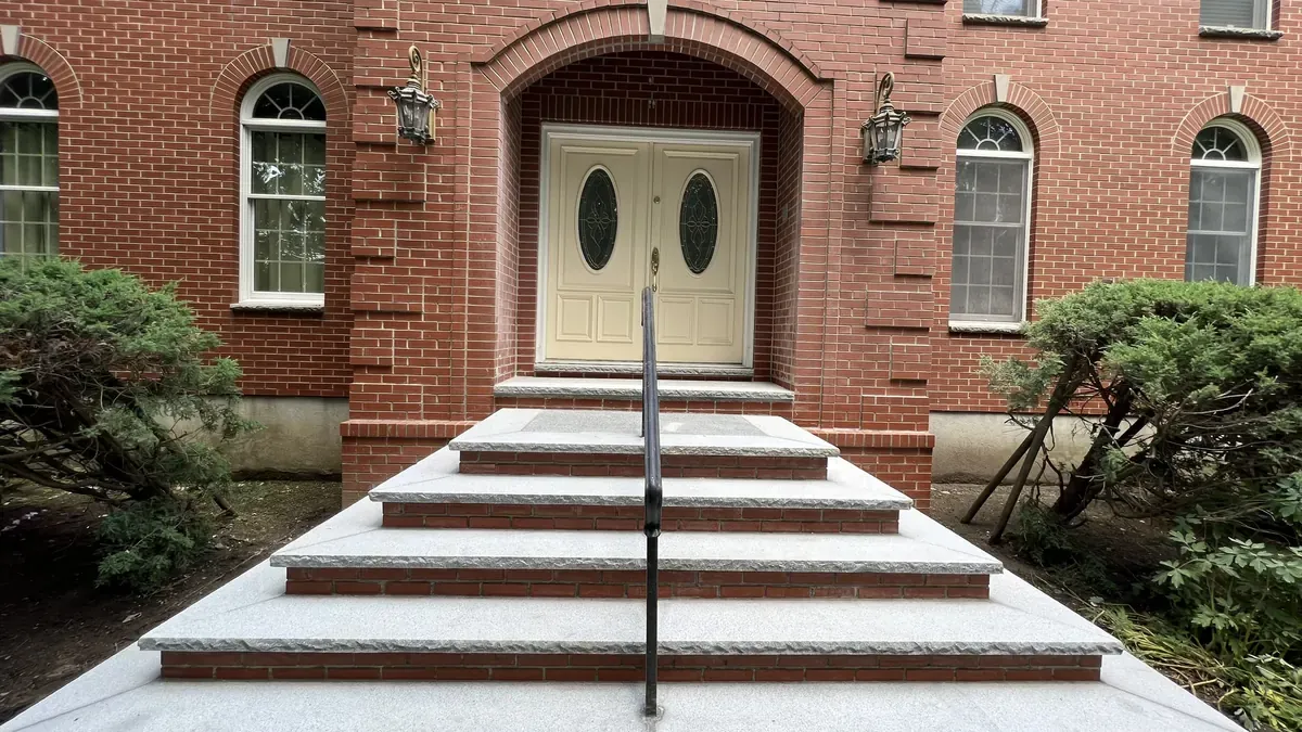 Wide granite front steps with a railing leading to a brick home