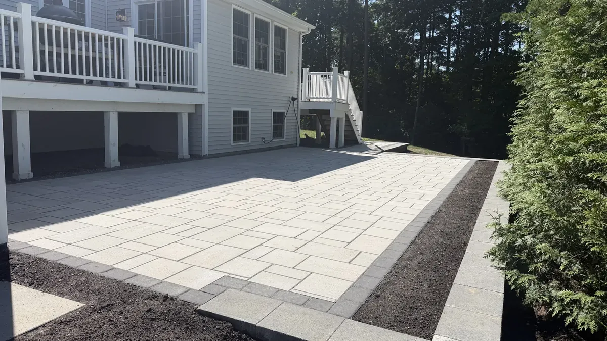 Large gray paver patio with a dark border behind a two-story house