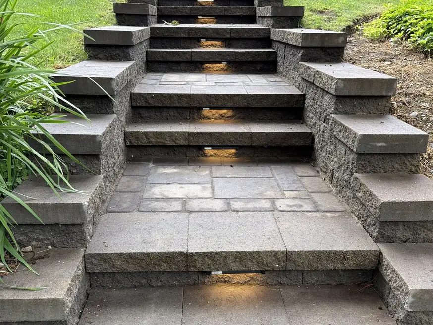 Stone masonry steps with built-in step lights leading up to a front lawn