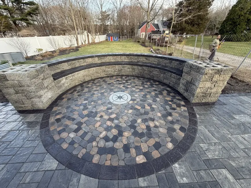 Paver patio with a circular cobblestone inlay framed by a curved stone seat wall