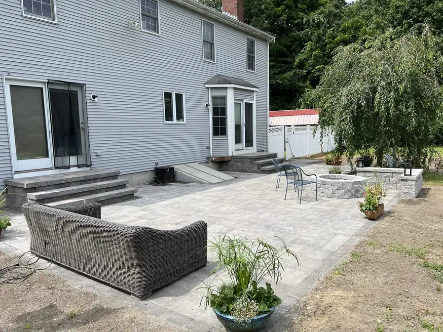 Paver patio with a round fire pit and a curved seat wall behind a house