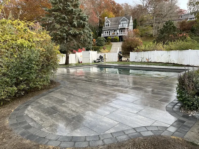 Gray paver pool deck with a curved dark border around an inground pool