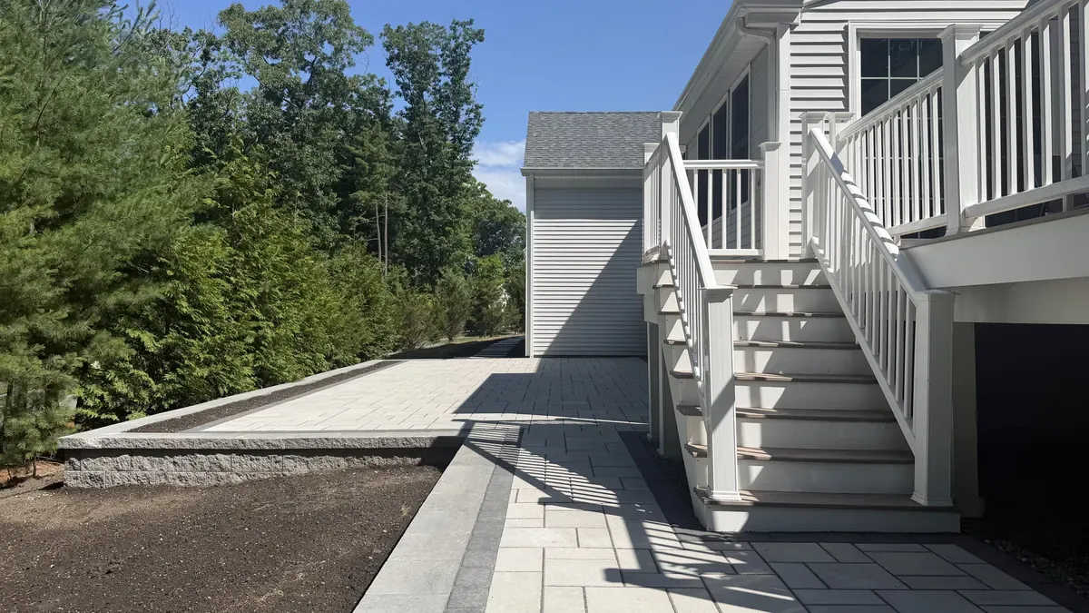 Paver walkway with a dark border leading to deck stairs beside a house