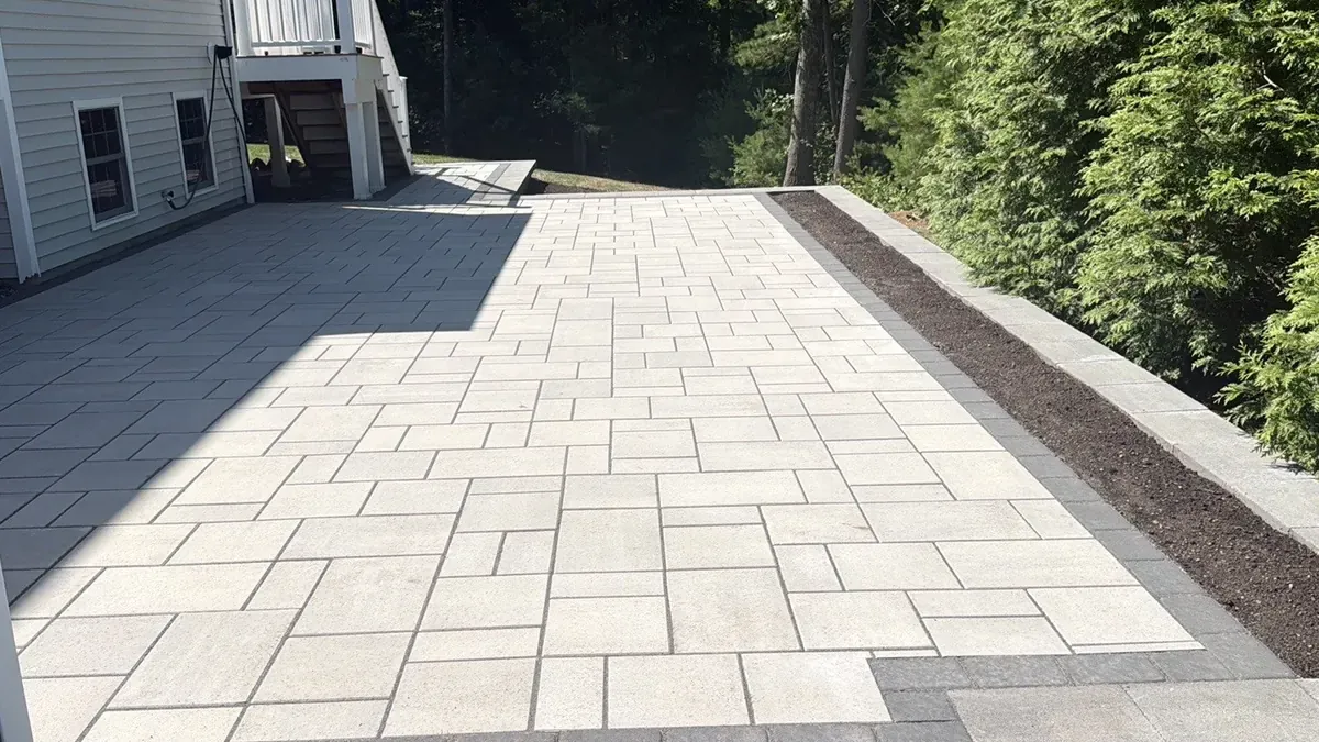 Large light gray paver patio with a dark border beside a house