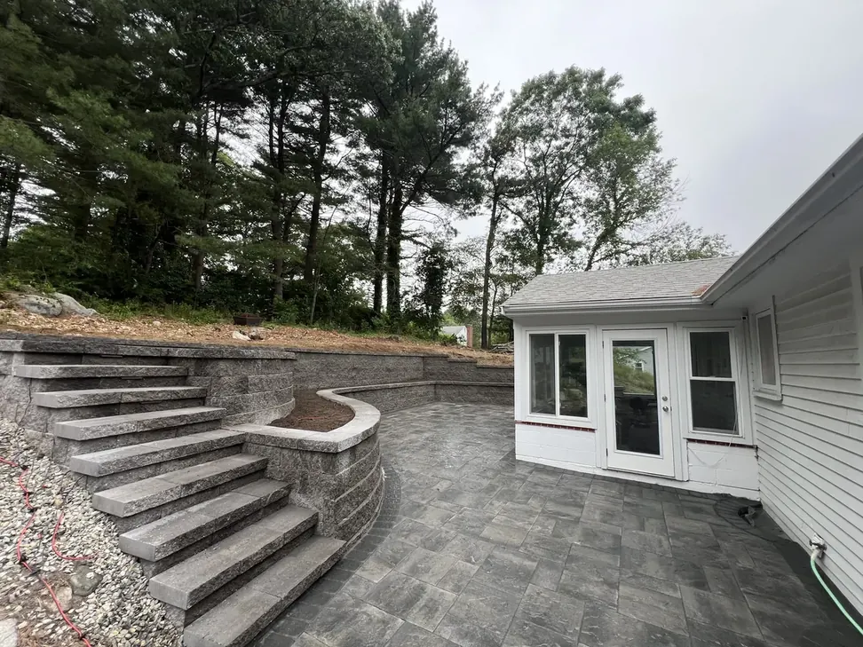 Terraced block retaining walls with stone steps and a paver patio behind a house