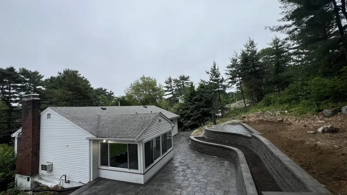 Curved block retaining walls and a paver patio beside a sunroom